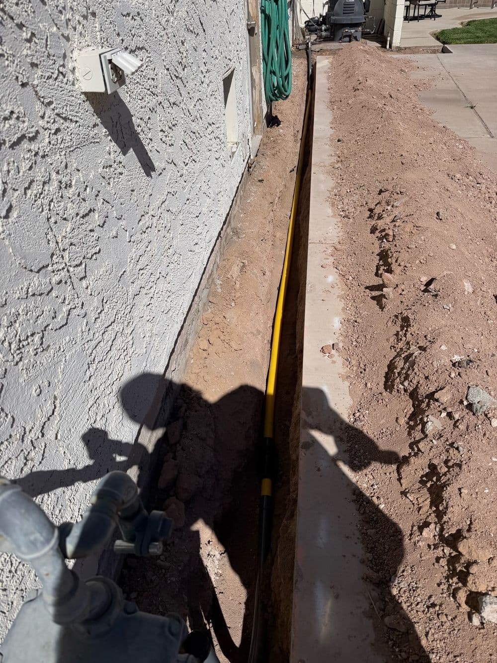 Yellow poly gas pipe laid in a trench along a stucco wall