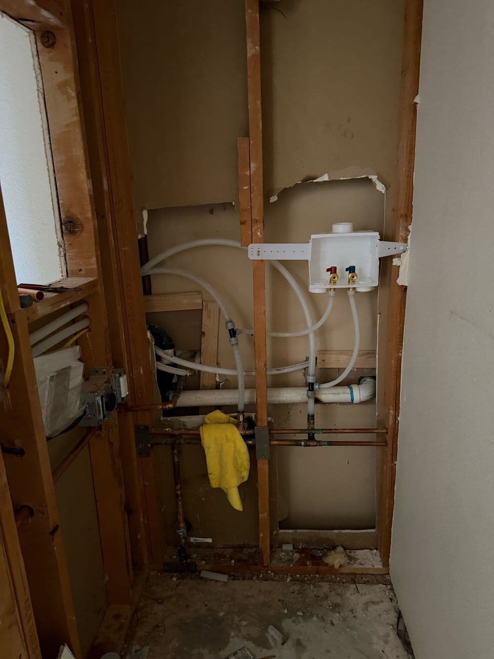 Laundry room wall open to the studs with new water lines and a washer box
